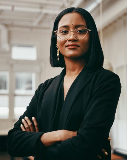 Woman power posing looking at the camera wearing black and glasses and has short hair
