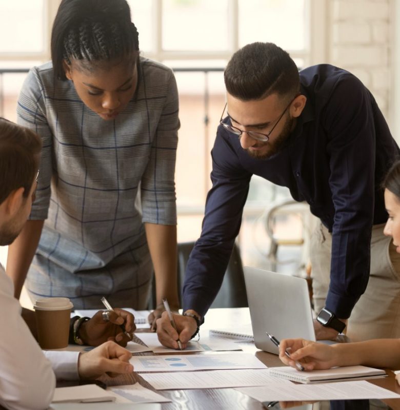 People working around a table. One man and one woman are standing and taking notes.